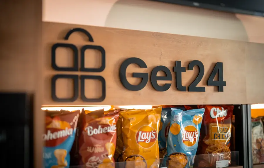 Logo GET24 na dřevěném čele micro-marketu nad policí se snacky