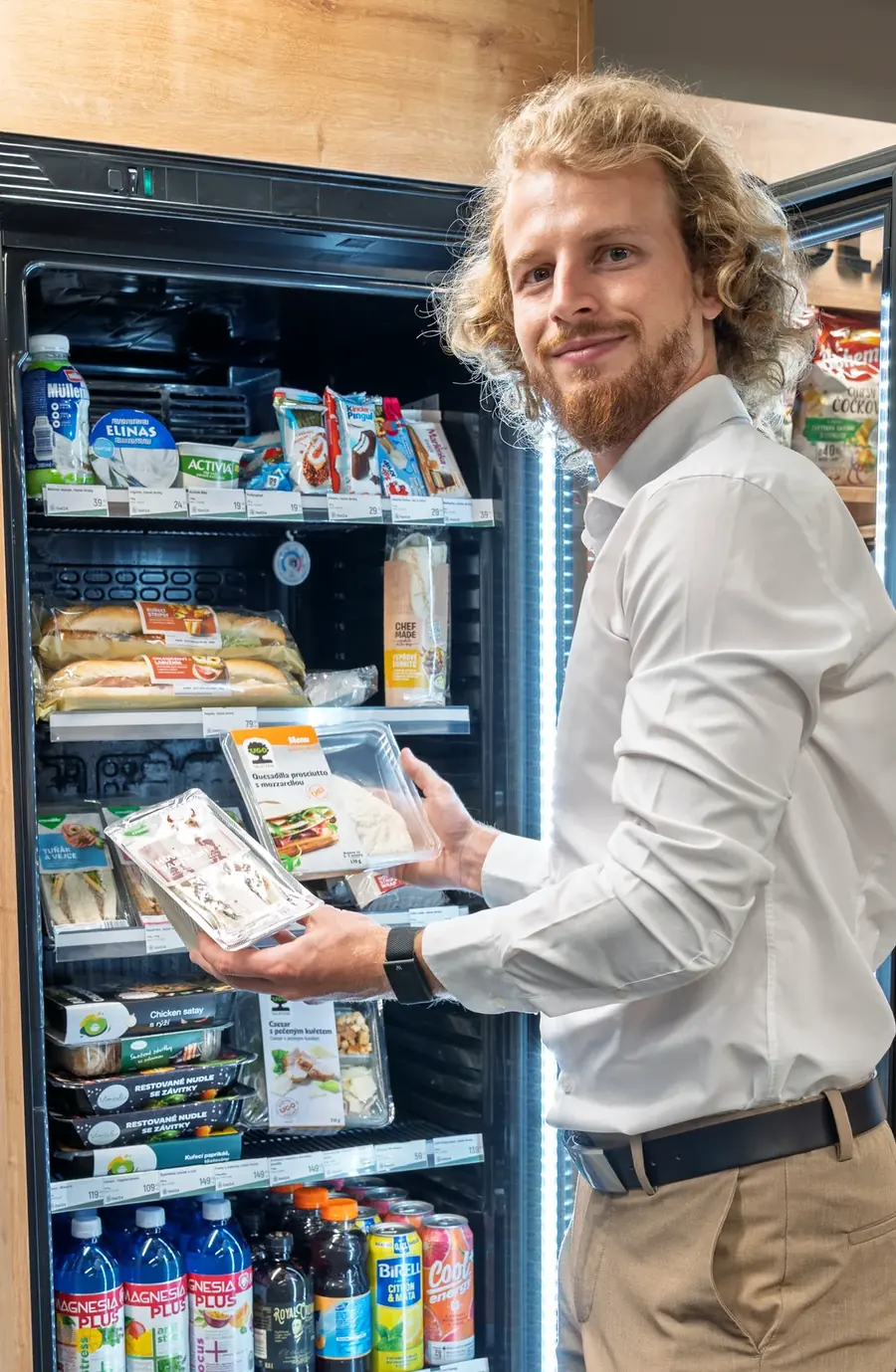 Zaměstnanec si vybírá hotové jídlo z chladicí vitríny micro-marketu